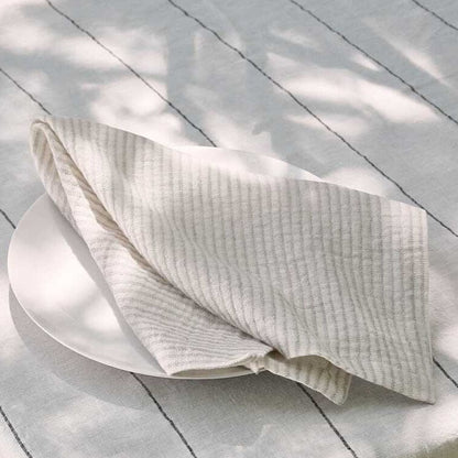 Folded white napkin on a white plate with a light wooden background