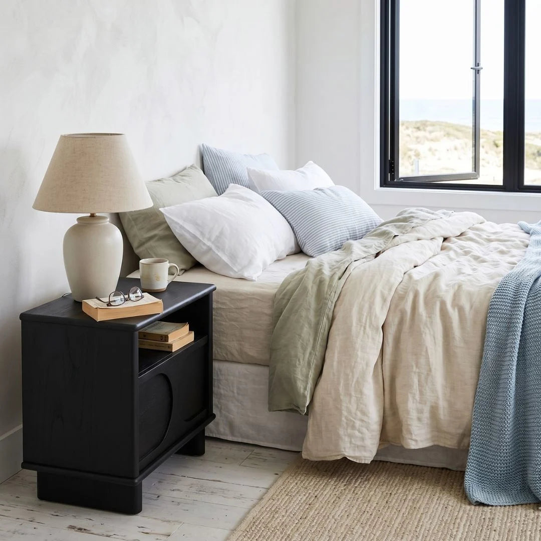 Bedroom with a black nightstand, lamp, and books near a bed with beige bedding.