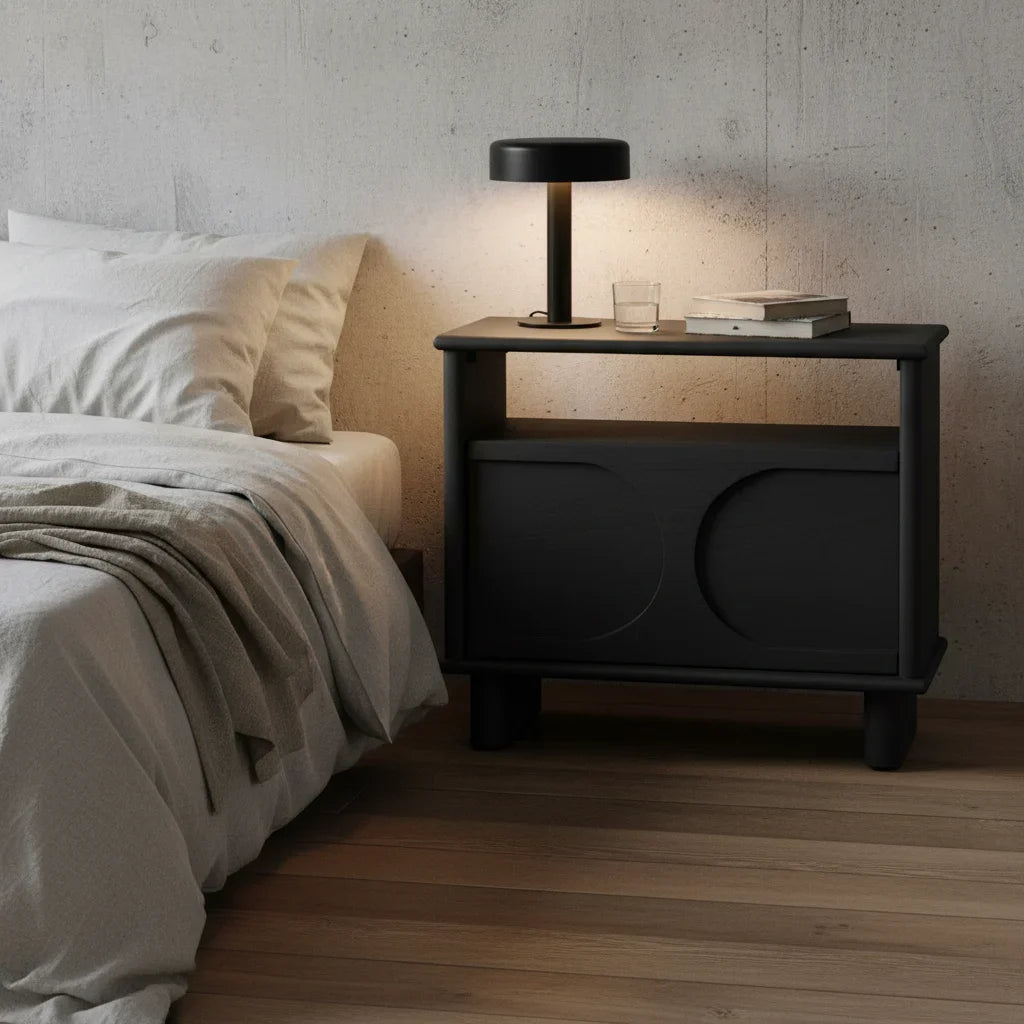 Black nightstand with lamp and glass next to a bed in a bedroom setting