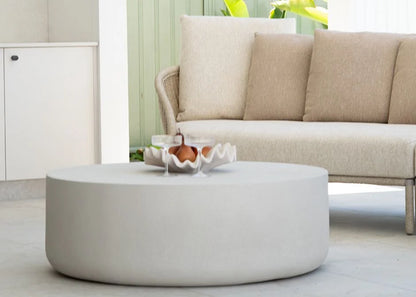 Round white coffee table in front of a beige sofa with decorative items on it.
