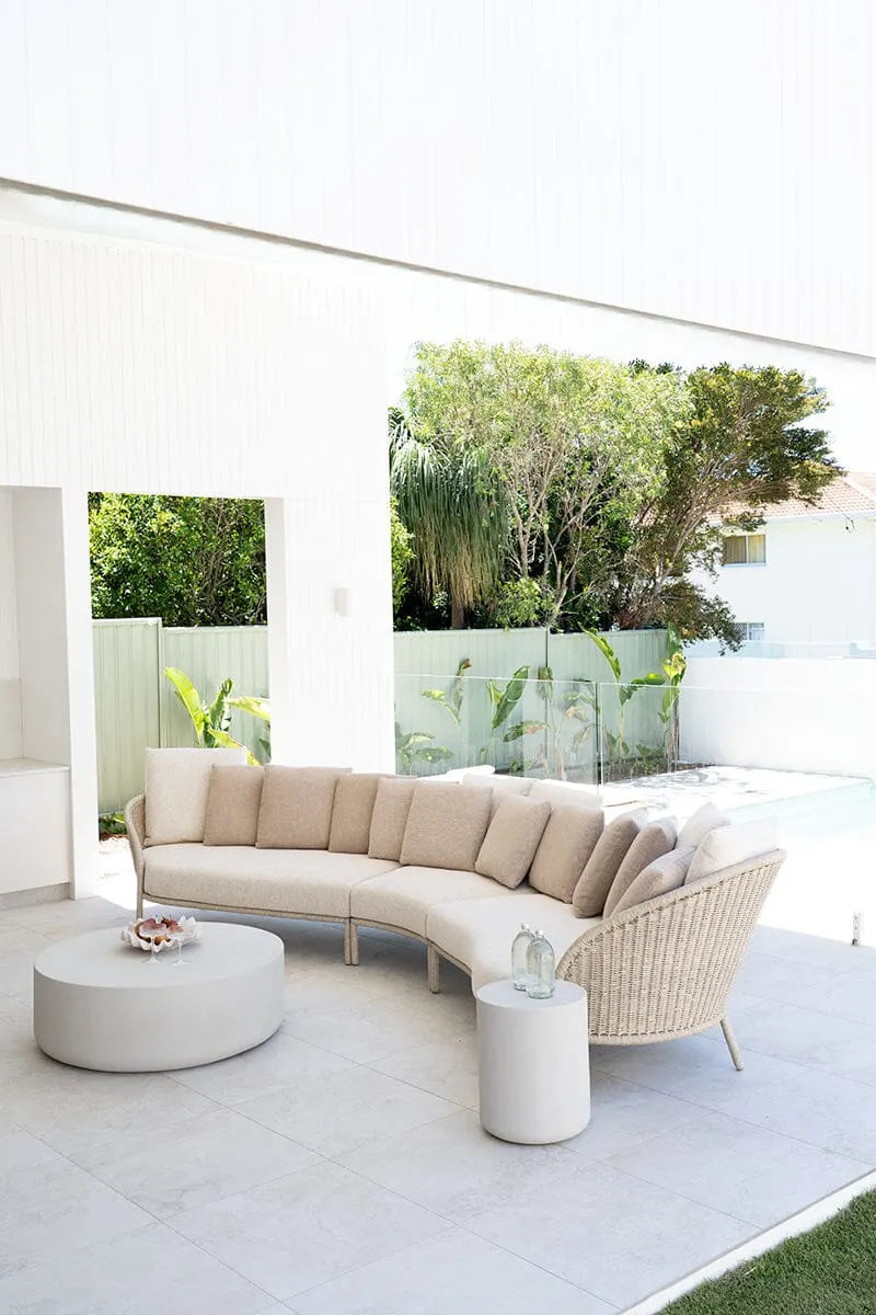 Modern outdoor furniture set with a curved beige sofa and wicker chairs on a patio.