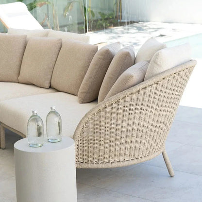 Beige outdoor sofa with wicker armrest and a small round table on a patio.