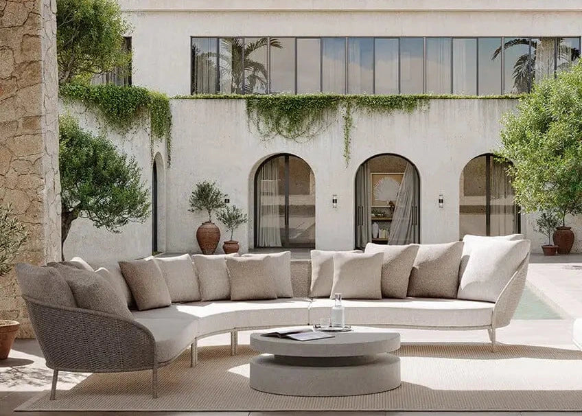 Modern outdoor seating area with a white sofa and coffee table in front of a building with arched windows and greenery.