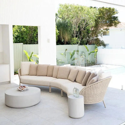 Modern outdoor furniture set with a curved beige sofa and wicker chairs on a patio.