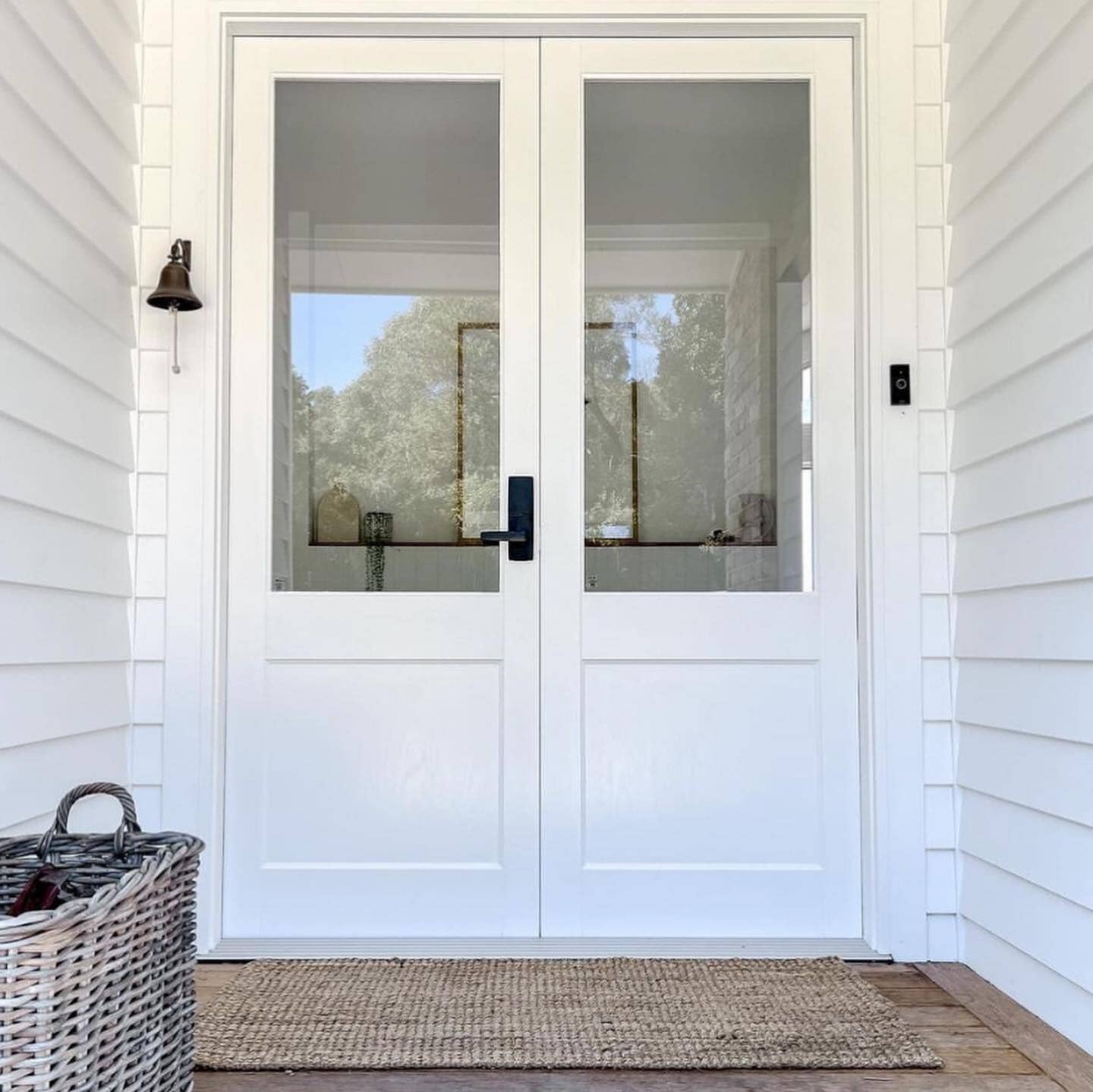 White double front door with glass panels, with natural jute door mat on a house exterior.
