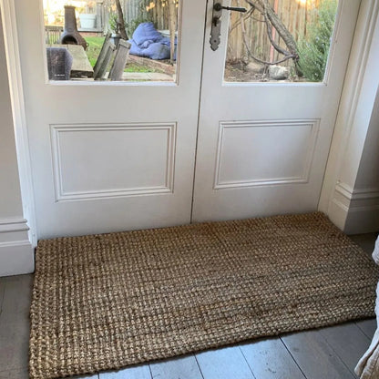 Natural Jute doormat in front of a white door with a view of a garden.
