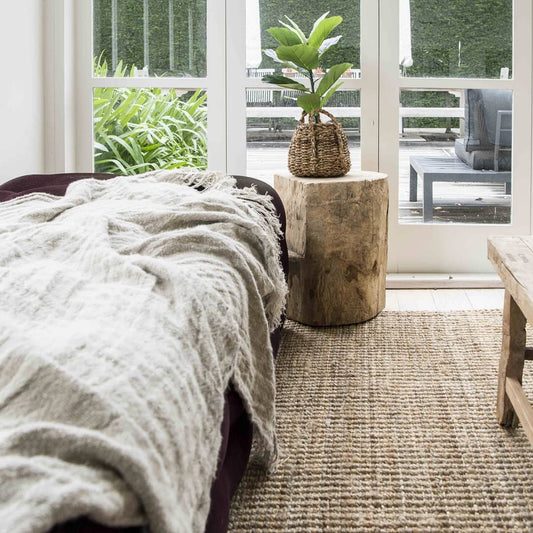 Cozy indoor setting with a bed, wooden side table, and plant in a woven basket.