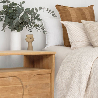 Wooden nightstand next to a bed with pillows and a plant