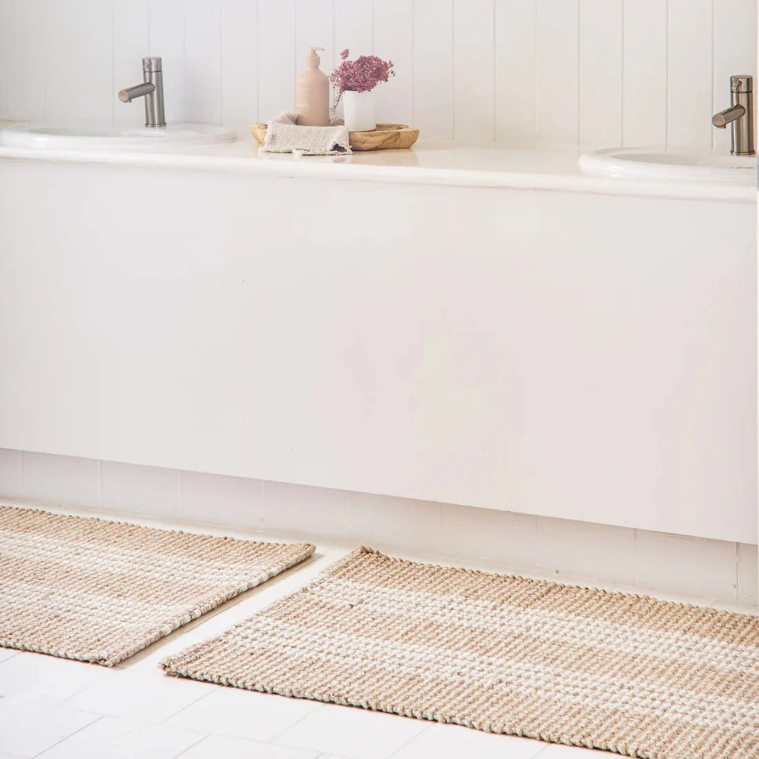 Two mats on a bathroom floor with a white bathtub and sink in the background.