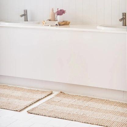 Two mats on a bathroom floor with a white bathtub and sink in the background.