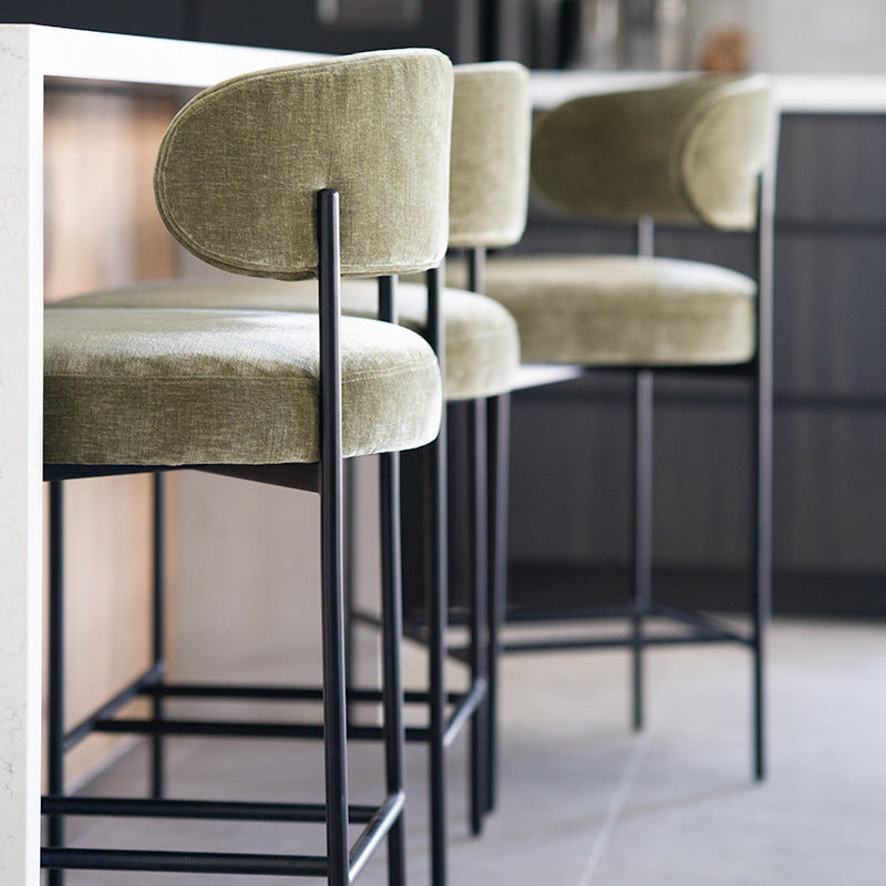 Three bar stools with green cushioned seats and black metal legs in a modern kitchen setting.
