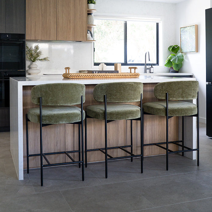 Modern kitchen with wooden cabinets, black appliances, and green bar stools.