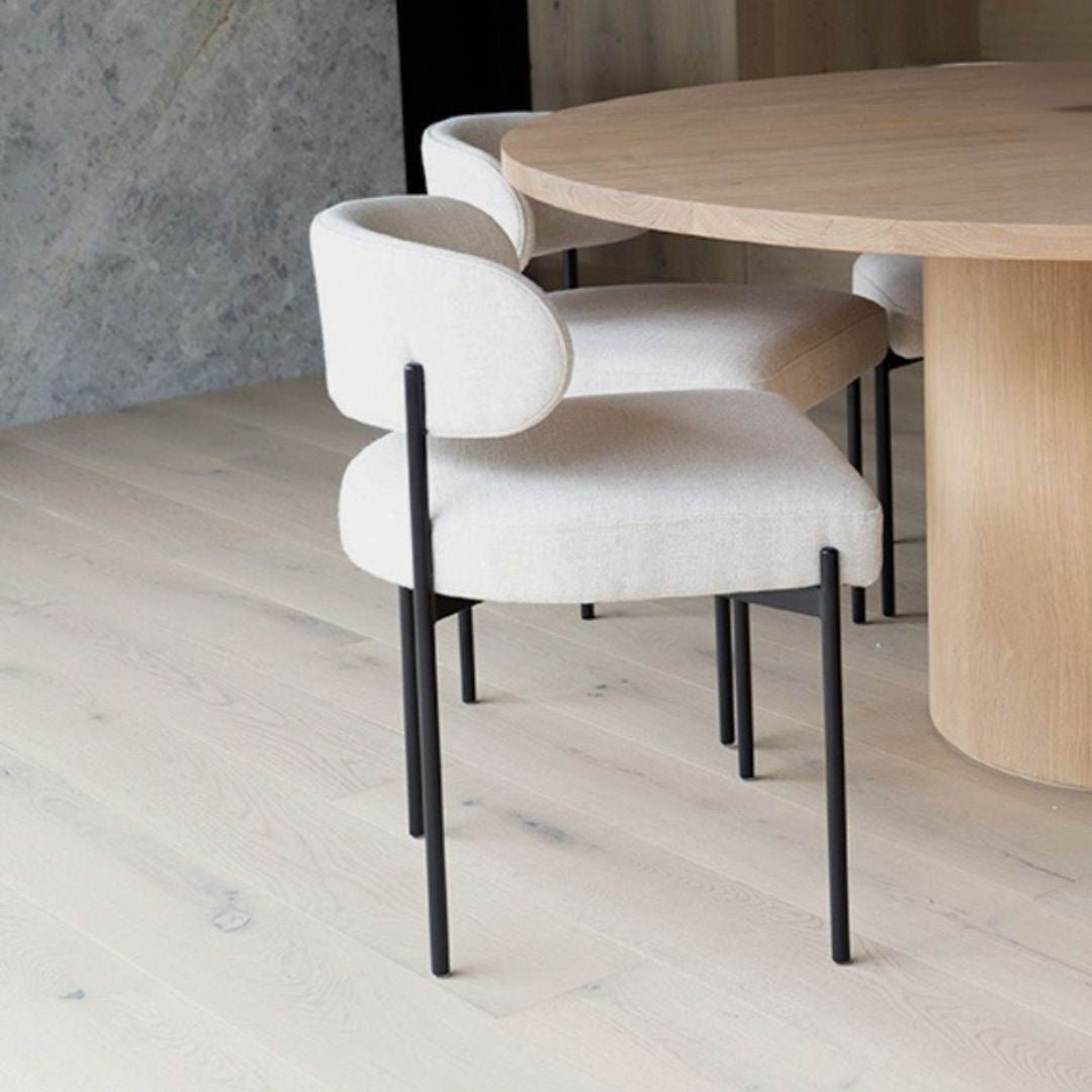 White chairs with black legs around a wooden dining table in a room with light wood flooring and a gray wall.