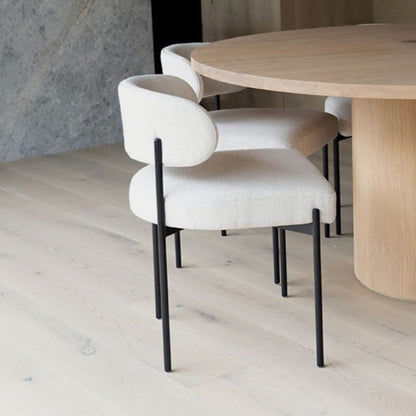 White chairs with black legs around a wooden dining table in a room with light wood flooring and a gray wall.