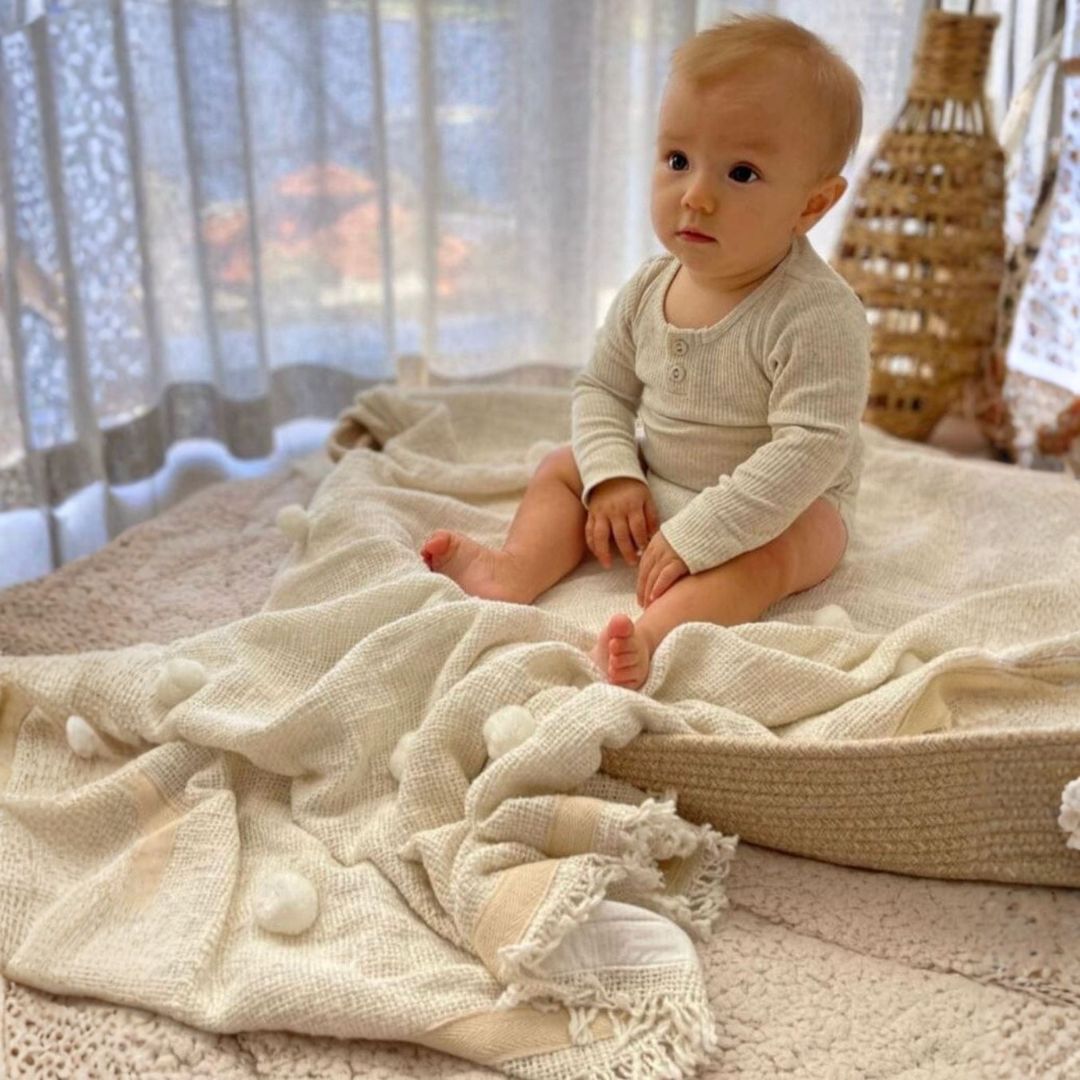Baby sitting on a textured blanket in a softly lit room