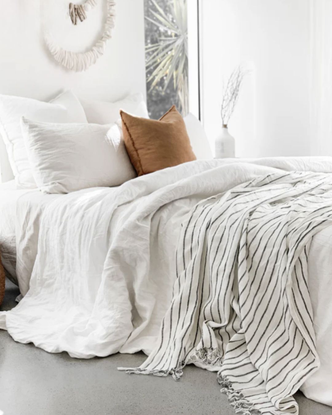 Neatly made bed with white bedding and a brown pillow in a bright bedroom.