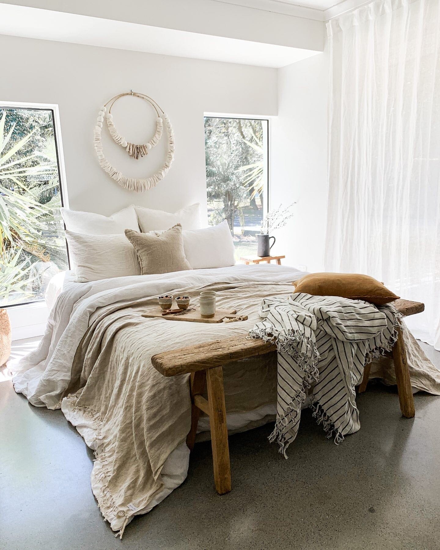 Cozy bedroom with a wooden bench, pillows, and a blanket in a bright room.