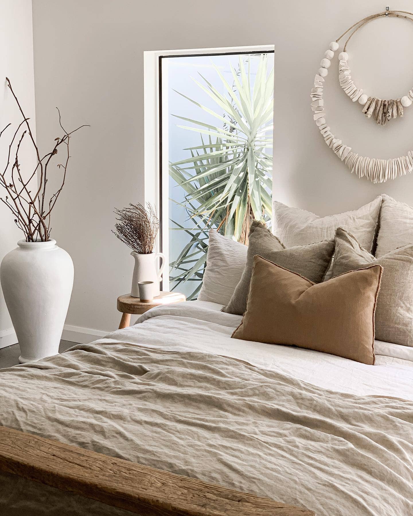 Neatly made bed with decorative pillows in a bedroom with a window and decorative wall piece.