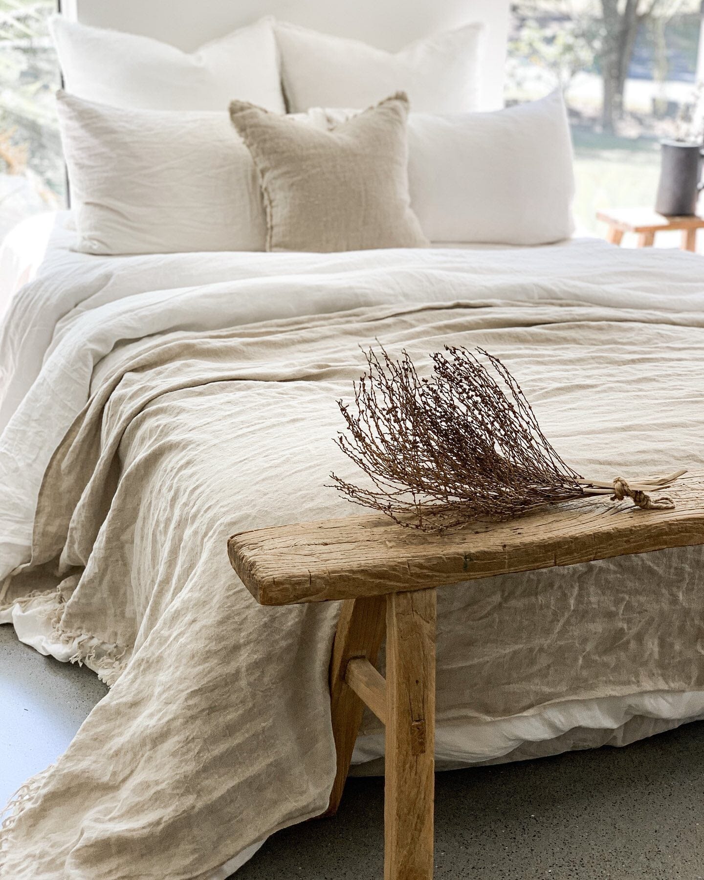 Beige bedding on a bed with a wooden bench and decorative branch in the foreground.