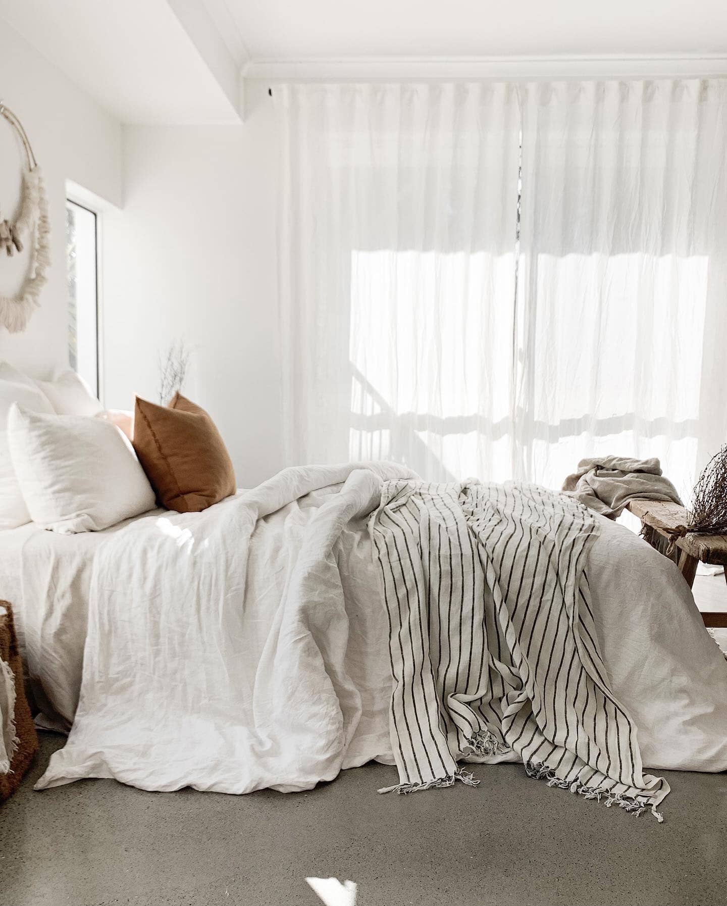 Cozy bedroom with a bed featuring white bedding and striped blanket, natural light filtering through curtains.