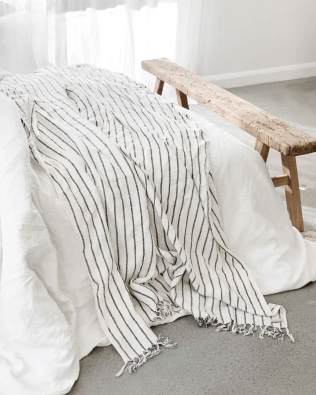 Striped blanket draped over a bed with a wooden bench in the background