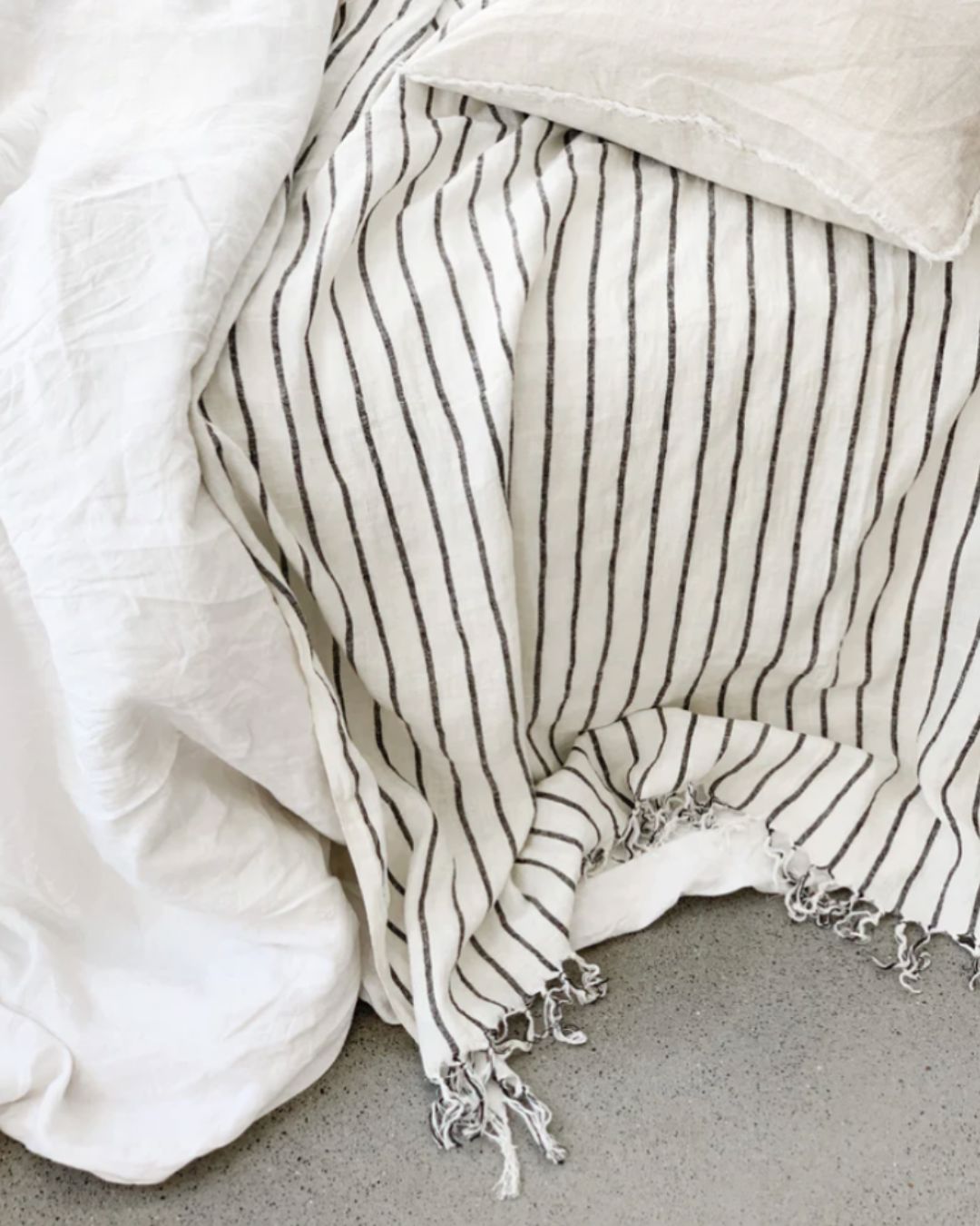 Striped towel with tassels draped over a white pillow on a neutral background