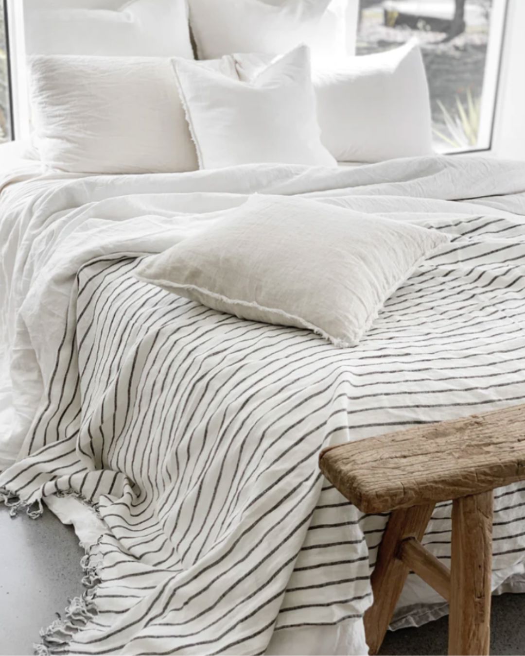 Neatly made bed with white bedding and a wooden bench in a bright room.