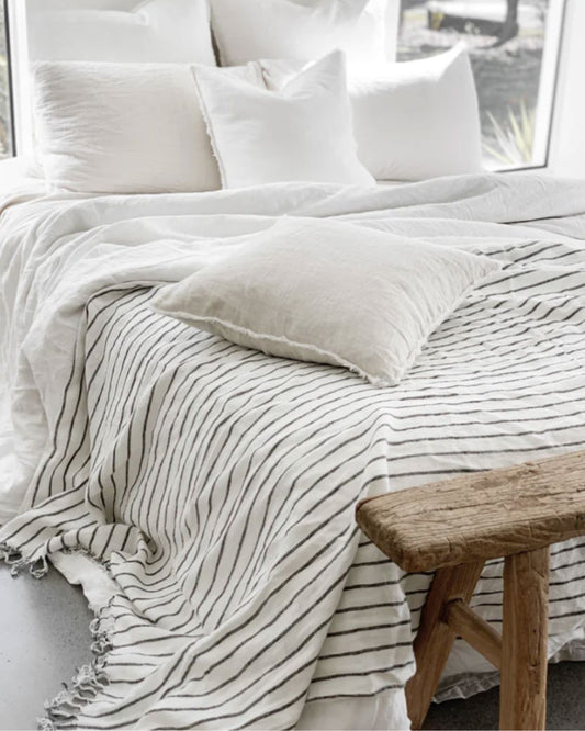 Neatly made bed with white bedding and a wooden bench in a bright room.