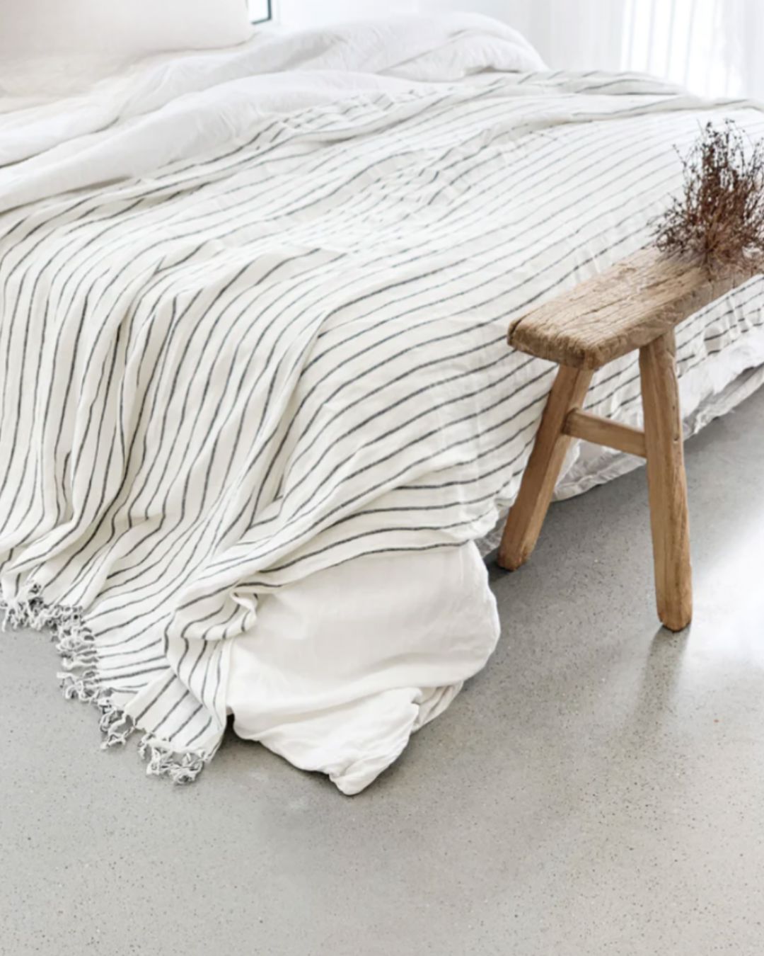 Textured white blanket draped over a bed with a wooden stool in a minimalistic room.