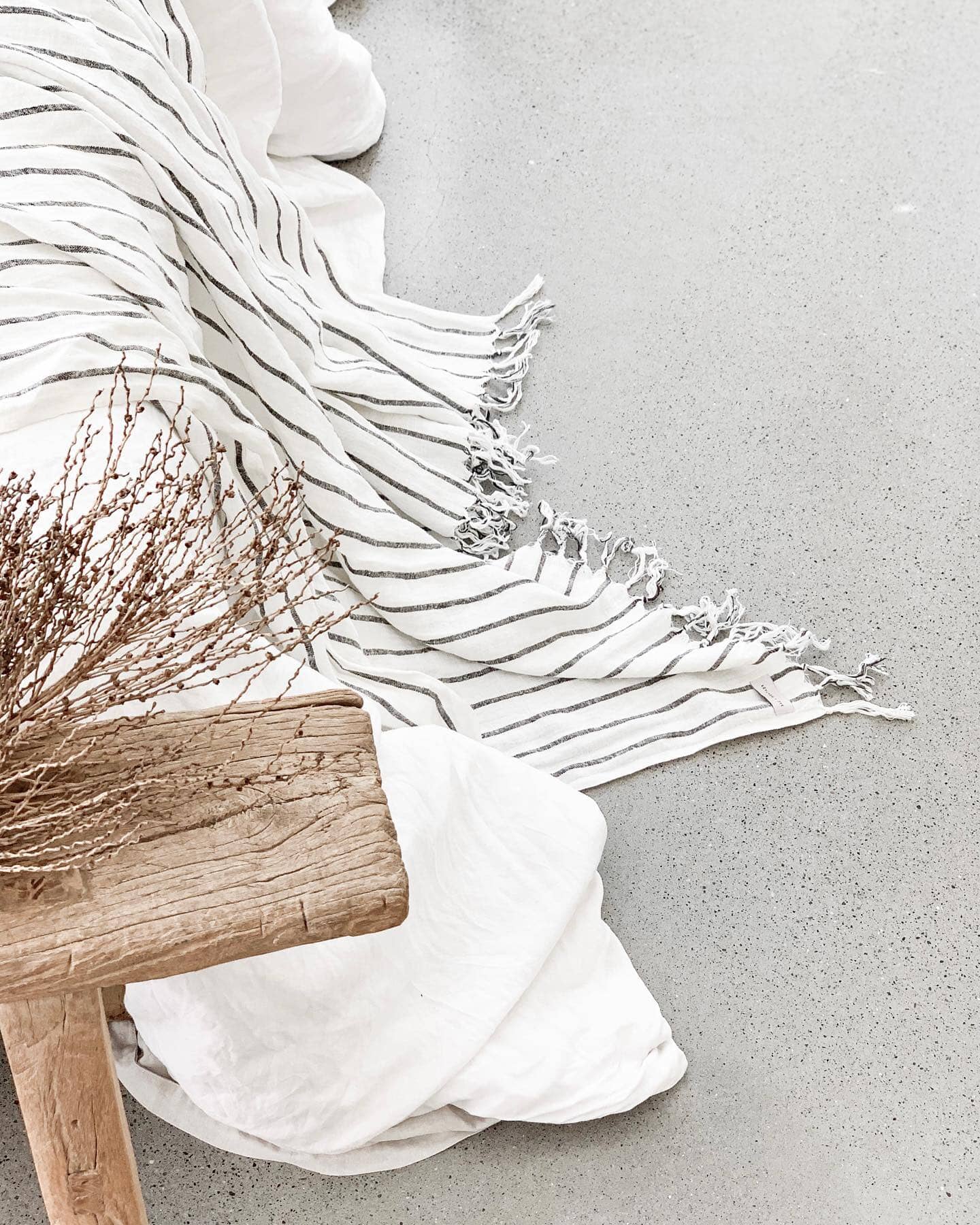 White fabric with fringes draped over a wooden stool on a light gray background