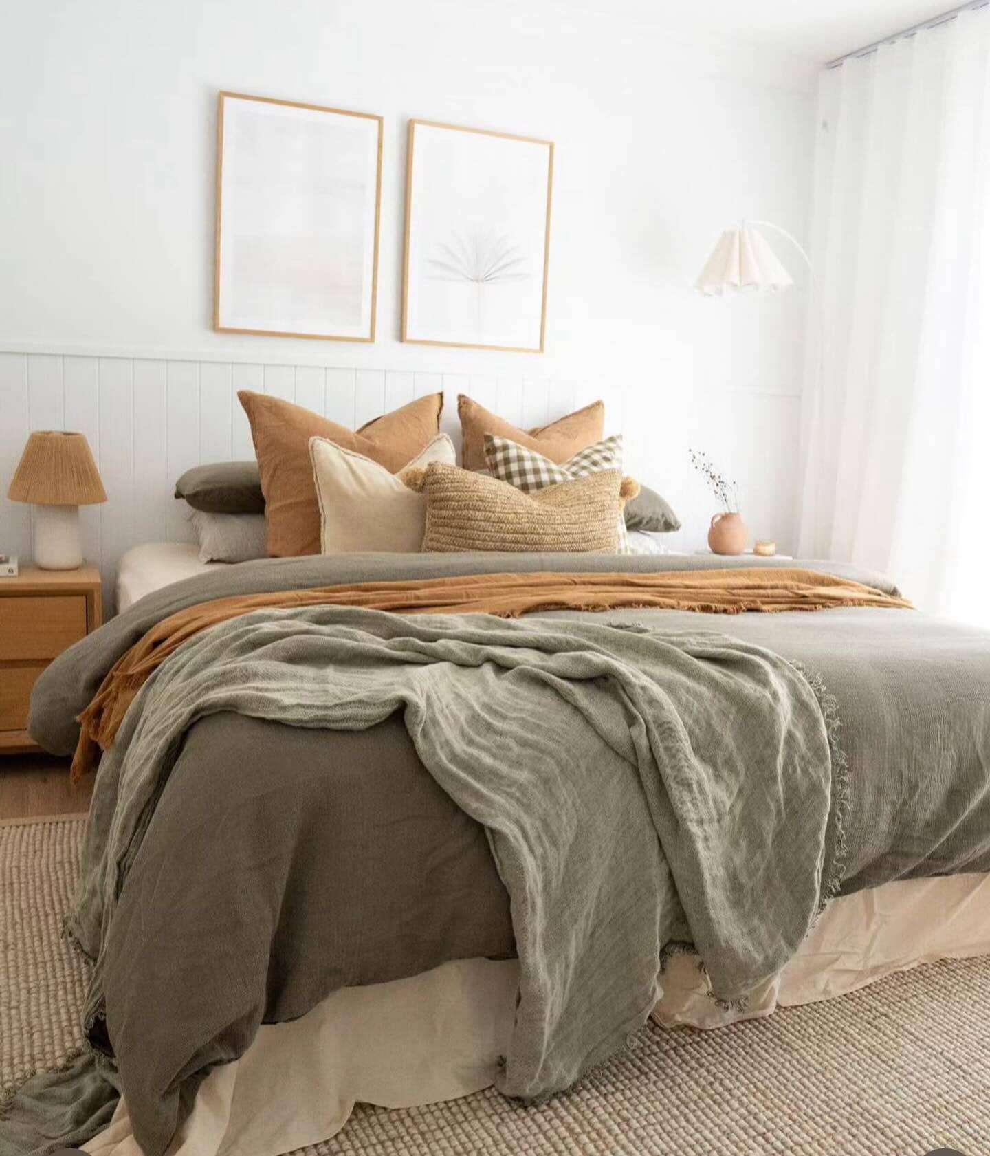 Cozy bedroom with a bed covered in green and brown blankets, pillows, and framed artwork on the wall.