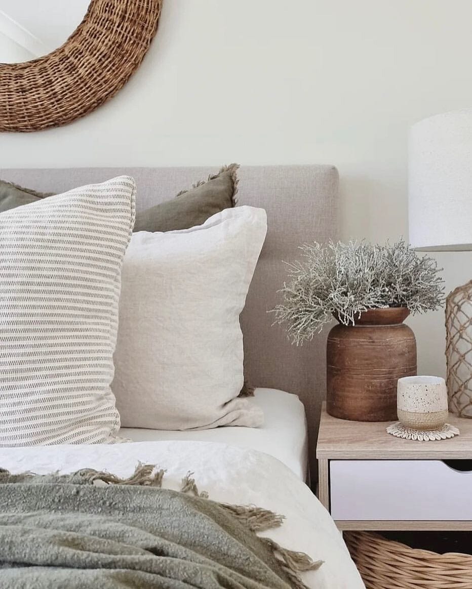 Neatly made bed with decorative pillows and a small plant on a nightstand.