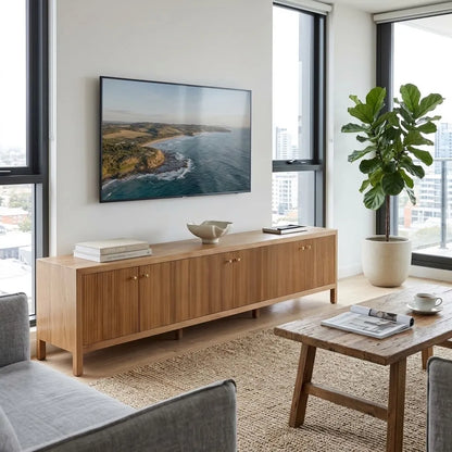 A modern light oak wood sideboard console cabinet in a bright, contemporary living room. The cabinet features vertical fluting on the doors, small round brass knobs, and a clean low profile.