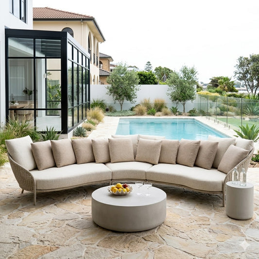 Outdoor patio setting with a curved sectional sofa and round coffee table by a pool.