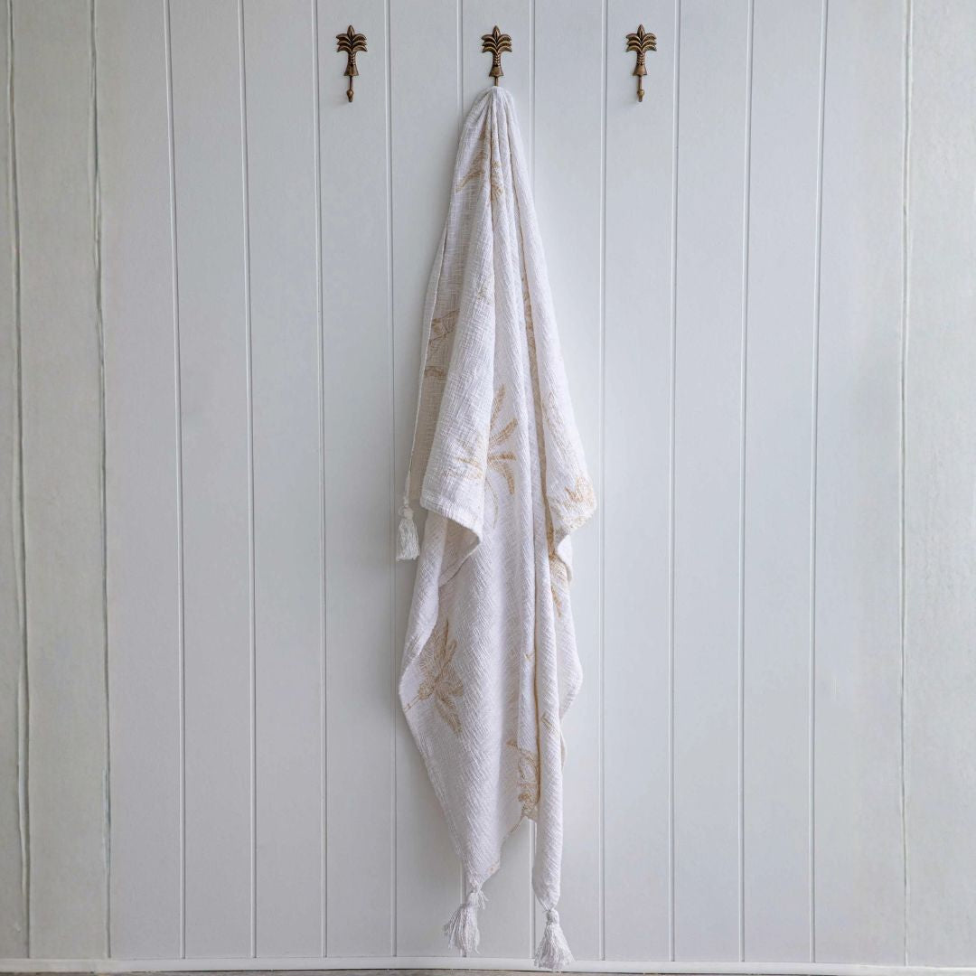 White towel with gold embroidery hanging on a wooden wall with hooks.