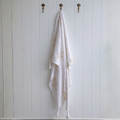 White towel with gold embroidery hanging on a wooden wall with hooks.