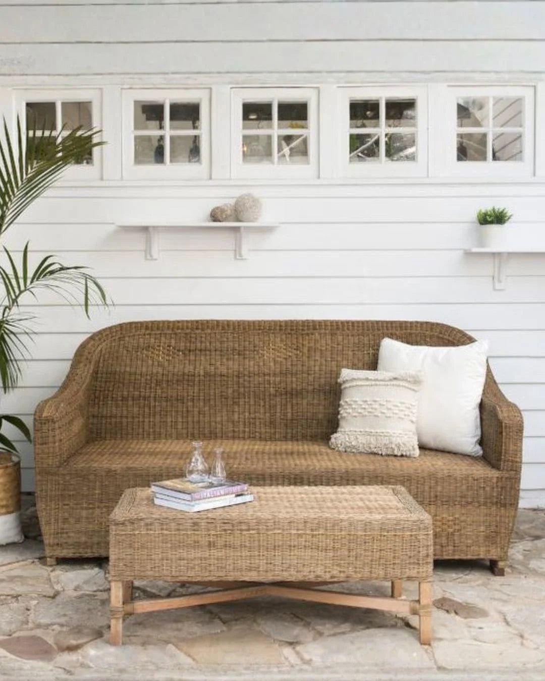 Wicker outdoor sofa with cushions on a patio area with a white building in the background.