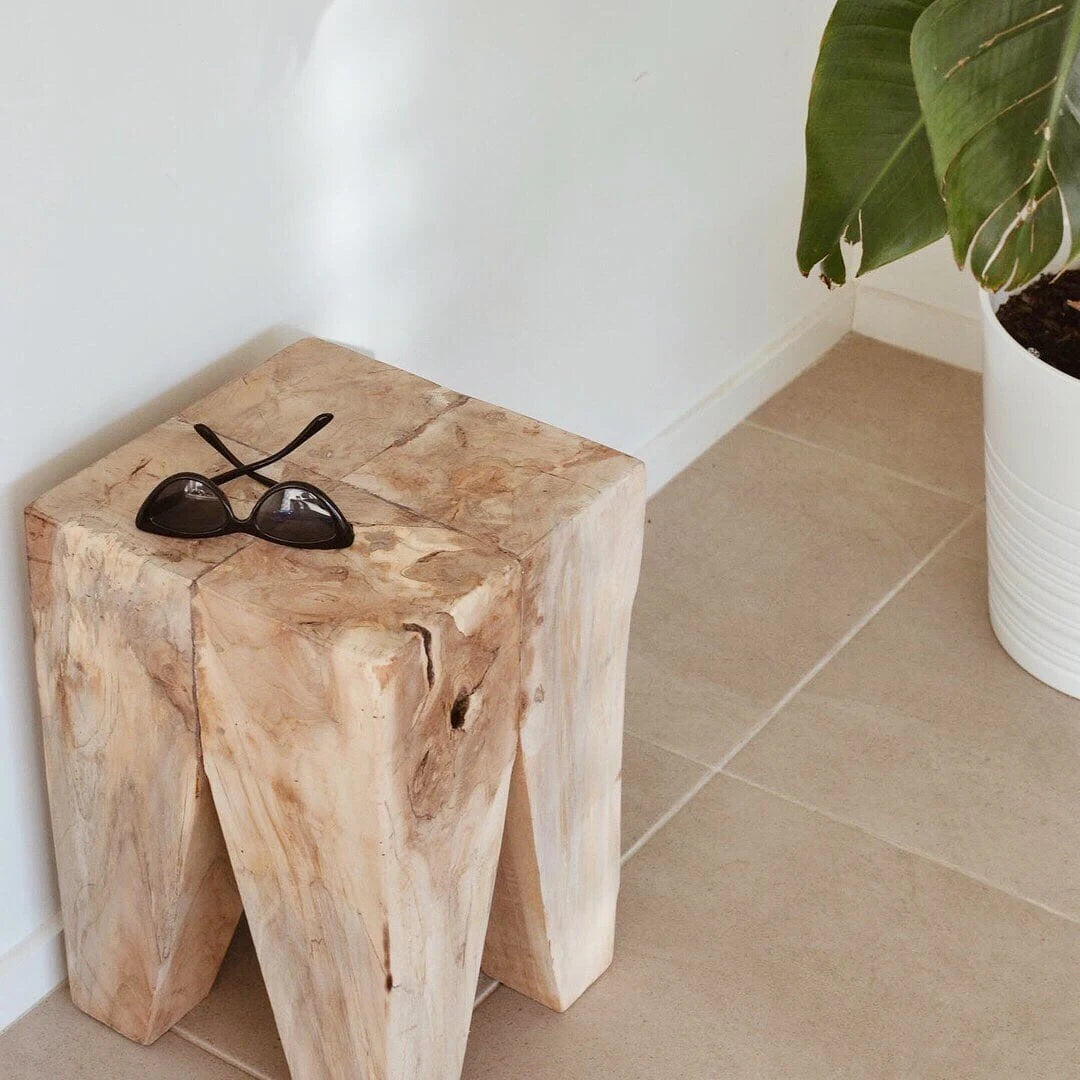 Teak peg stool with sunglasses on a tiled floor next to a plant