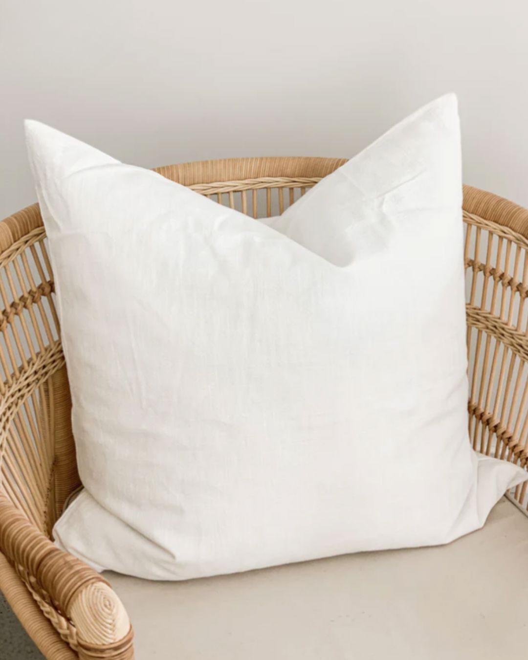 White pillow on a wicker chair with a neutral background