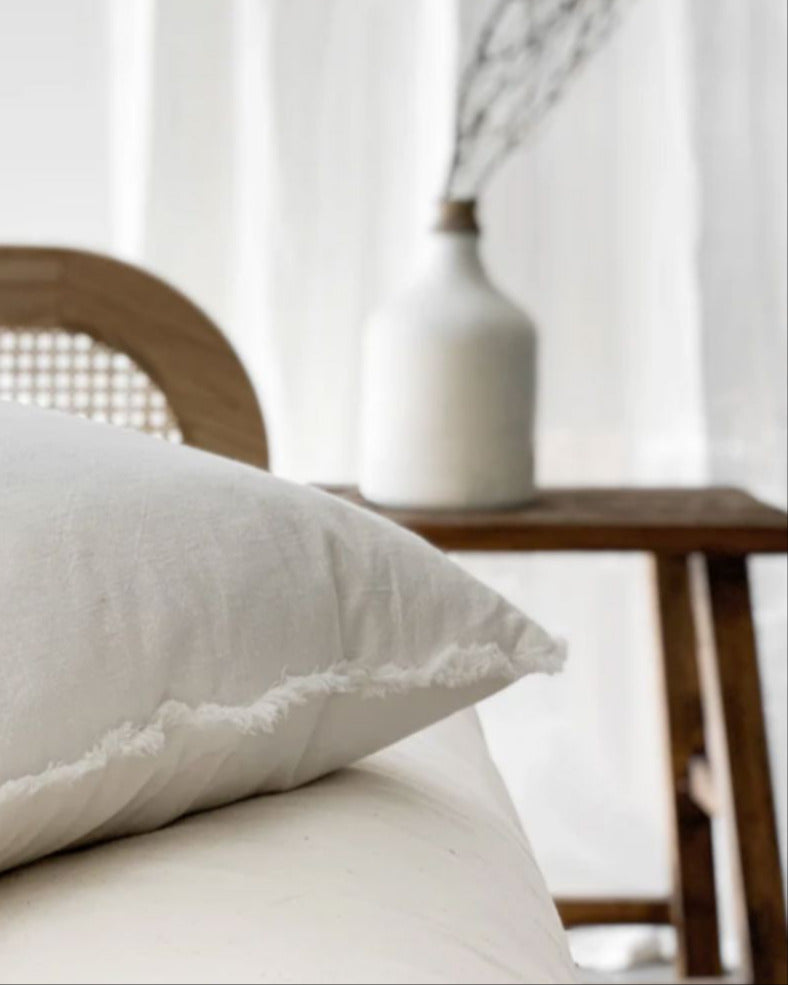 Chalk white ramie cushion cover with hand-finished fringe edges on modern neutral sofa