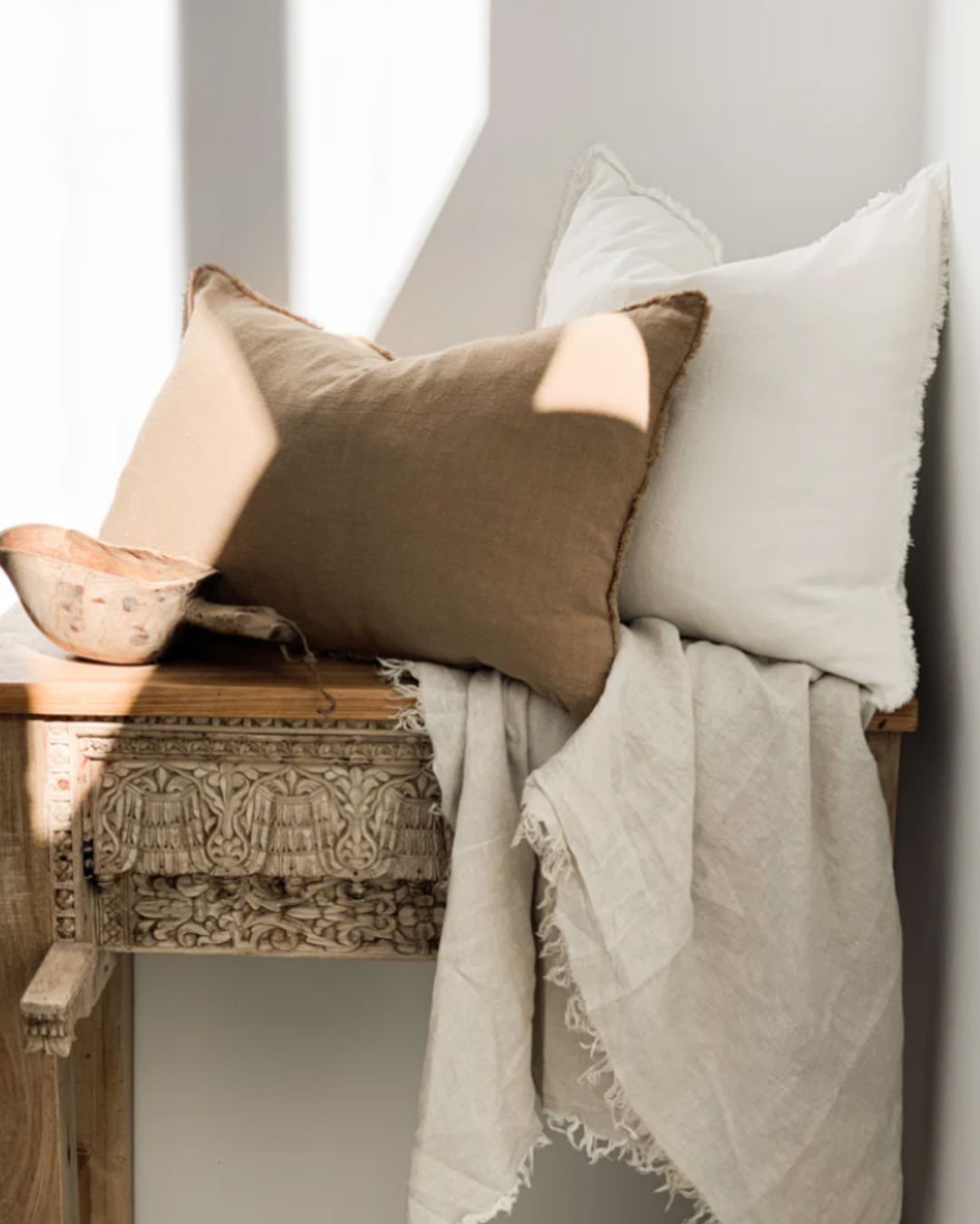 Decorative pillows and blanket on a wooden bench against a white wall