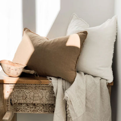 Decorative pillows and blanket on a wooden bench against a white wall