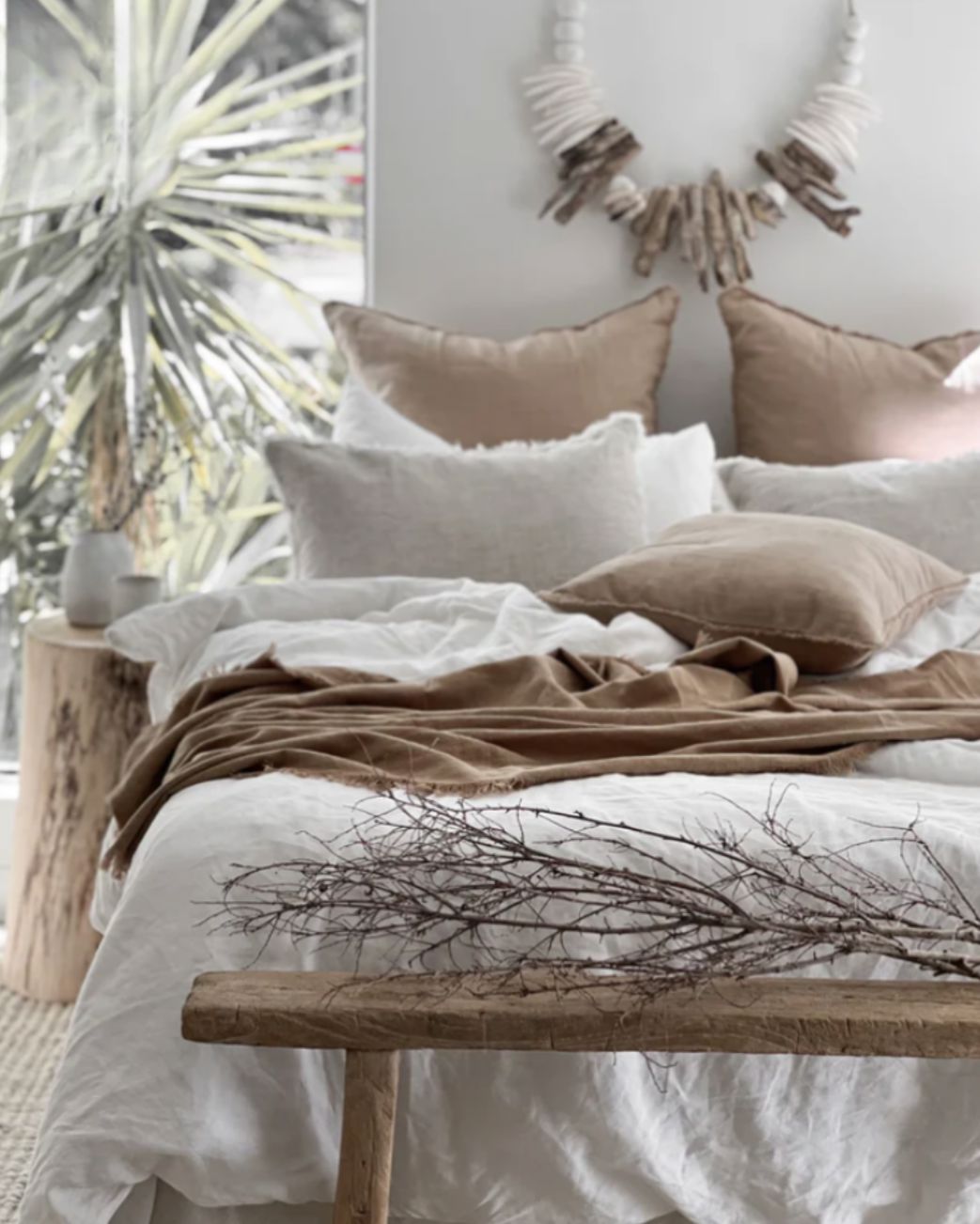Cozy bedroom with neutral tones, pillows, and a wooden bench.