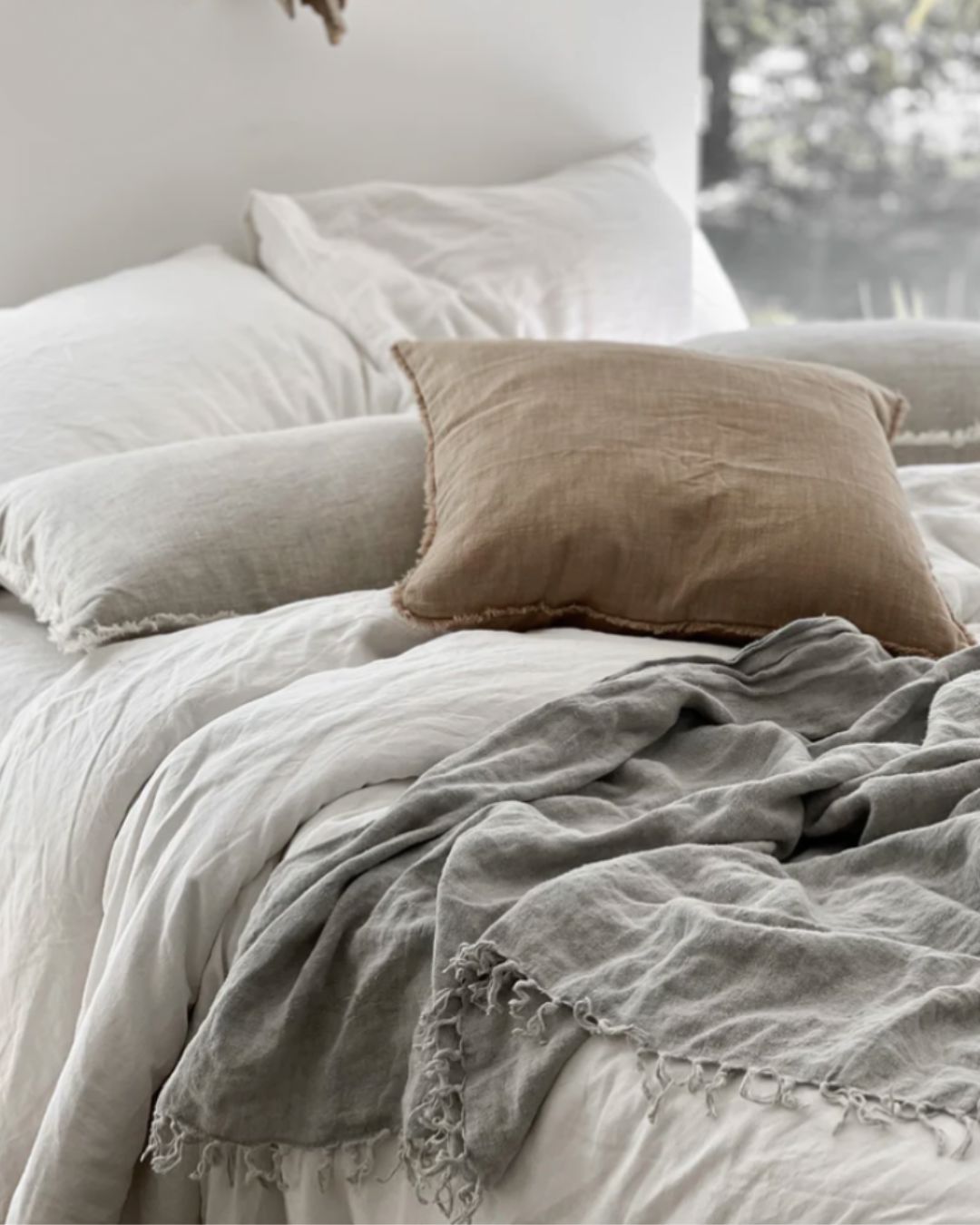 Neatly made bed with light-colored bedding and a brown pillow.