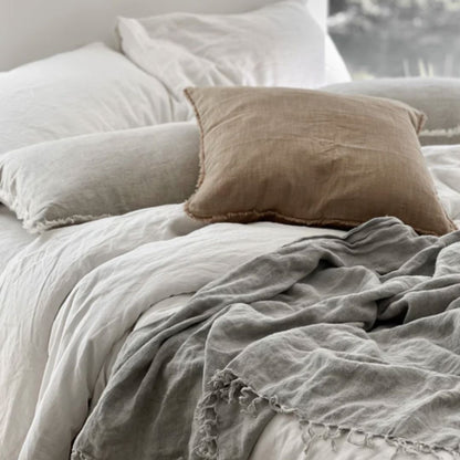 Neatly made bed with light-colored bedding and a brown pillow.