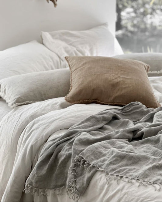 Neatly made bed with light-colored bedding and a brown pillow.