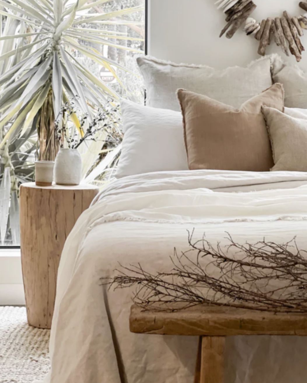 Neatly made bed with beige and white bedding in a bright room with plants.