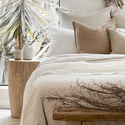 Neatly made bed with beige and white bedding in a bright room with plants.