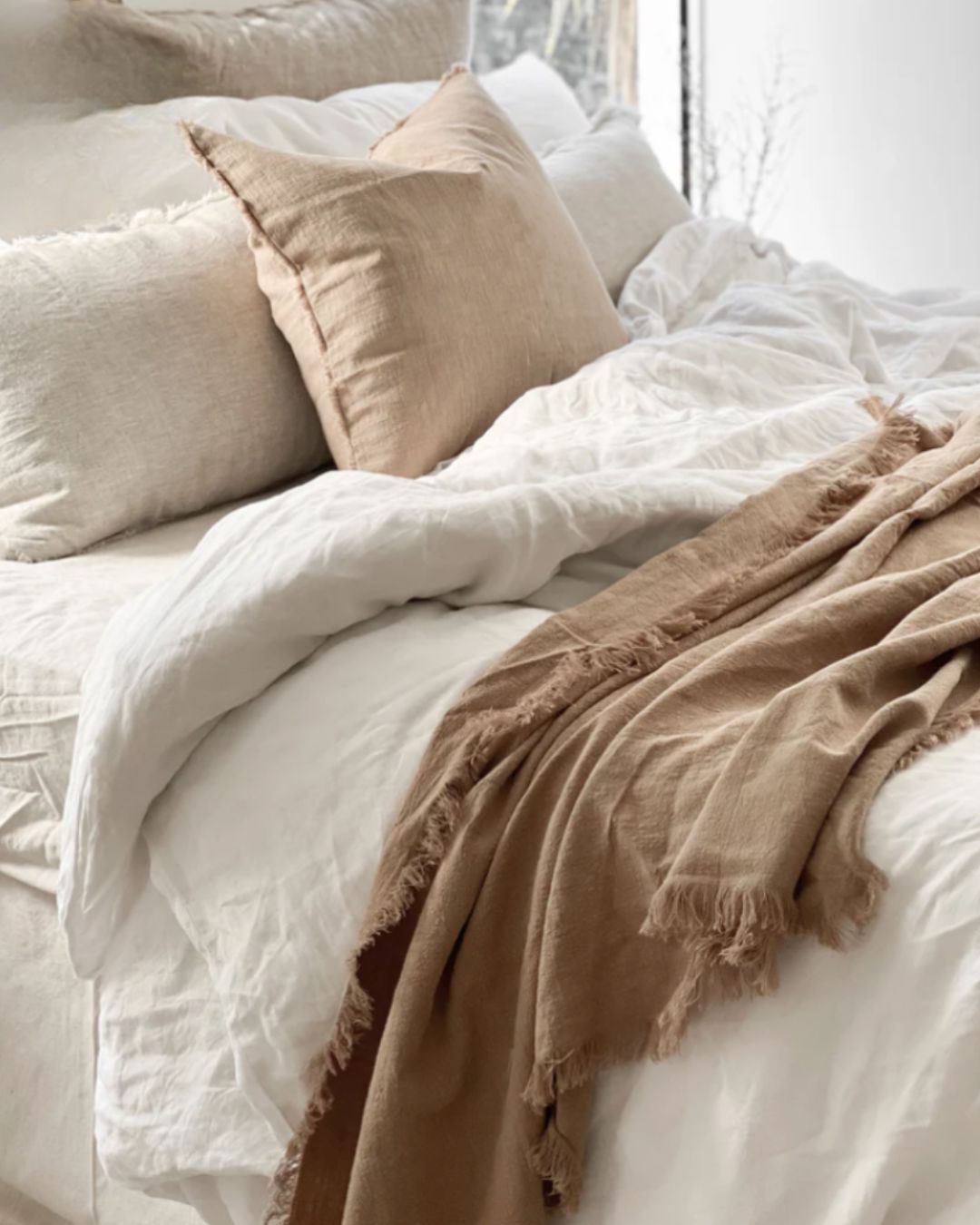 Neatly made bed with white bedding and beige pillows and throw blanket.