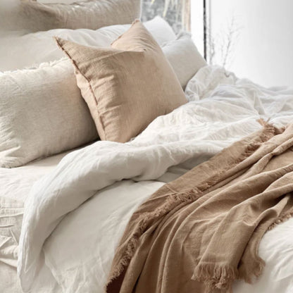 Neatly made bed with white bedding and beige pillows and throw blanket.